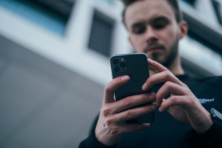 黒セーターを着てスマートフォンでSNSのコーデを見るメンズ
