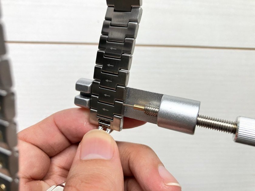バンド万力に腕時計のブレスをセットし、ピン抜き棒で矢印方向にピンを押す